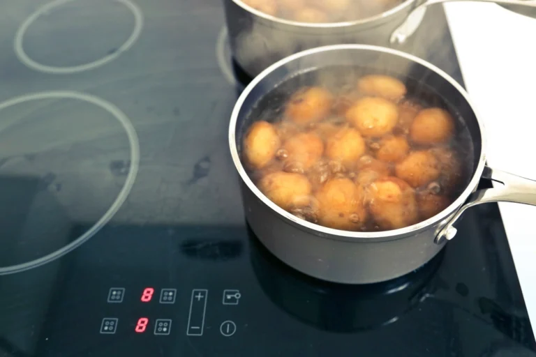 Black glass-ceramic cooktop with digital touch controls and a pan of potatoes at a rolling boil